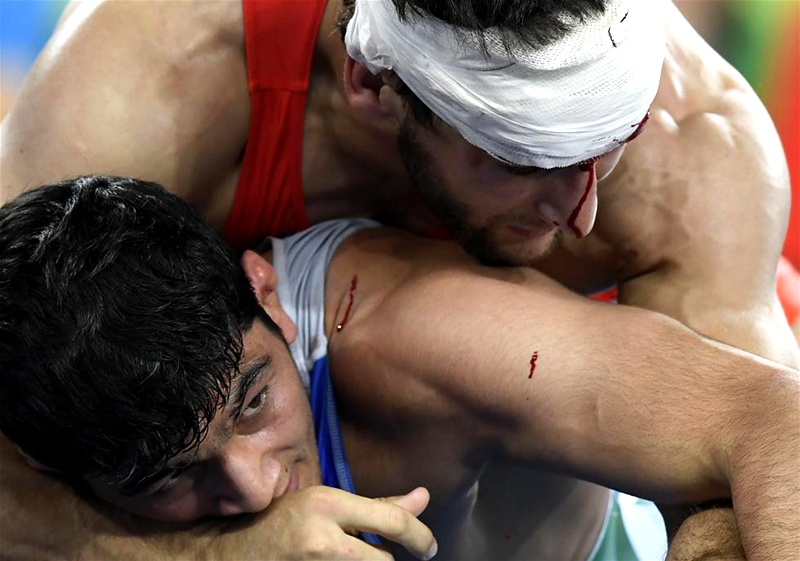 巴西当地时间8月19日下午，在2016里约奥运会摔跤男子自由式74公斤级决赛中，俄罗斯选手杰杜耶夫眼眶受伤，头部缠上绷带坚持比赛，最终负于伊朗选手亚兹达尼查拉提，屈居亚军。图为俄罗斯选手杰杜耶夫（上）与伊朗选手亚兹达尼查拉提在比赛中。新华社记者武巍摄