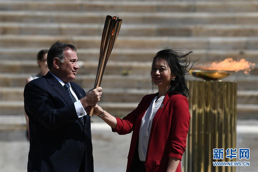 日本代表團成員井本直步子（右）從希臘奧委會主席斯皮羅斯·卡普拉洛斯手中接過東京奧運會聖火火炬。